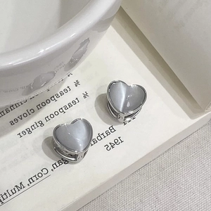 Macro shot of silver heart-shaped cat-eye stone earrings on a minimalist white book