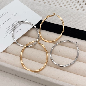 Twisted metal hoop earrings in gold and silver finish displayed on a jewelry tray