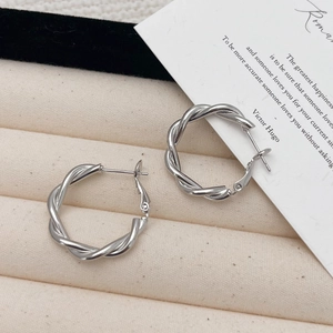 Créoles torsadées en argent poli sur un plateau à bijoux texturé de couleur crème