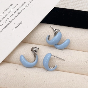 Detailed close-up of light blue enamel C-shaped earrings on a textured jewelry display pad