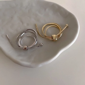 Close-up of adjustable gold and silver snake chain rings on a minimalist ceramic plate