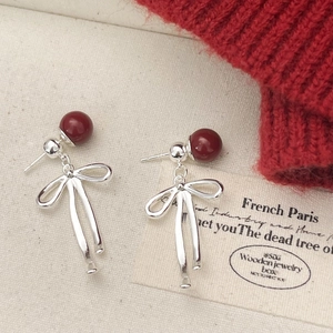 Detailed view of silver bow earrings with a deep red bead in a French vintage style
