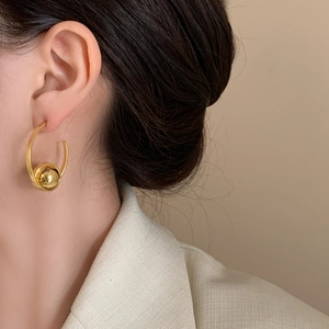 Minimalist C-shaped gold hoop earrings with sliding bead on model with beige background