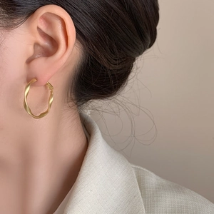 Minimalist geometric twisted gold hoop earrings shown on a model in a side-view close-up shot