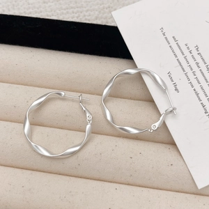 Macro shot of matte silver twisted hoop earrings with satin finish on beige velvet tray