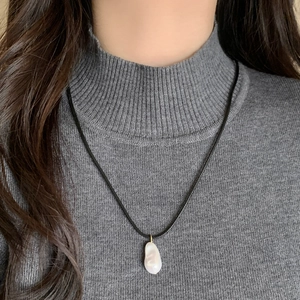 Pendentif perle baroque sur collier en cordon de cuir noir sur pull gris