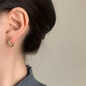 Elegant gold hoop earrings with fine grain texture worn with a casual grey knit top