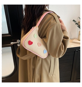 Detail of woven beige underarm bag with pink trim and colorful heart patch embroidery