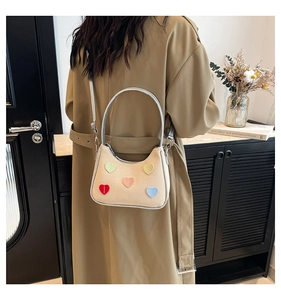 Detail of cream woven shoulder bag featuring colorful heart patches and silver accents