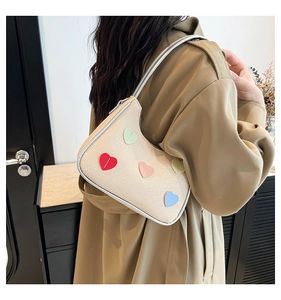 Detail of woven beige shoulder bag featuring colorful heart patches and silver trim