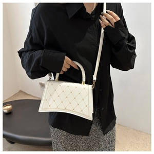 Close-up of white quilted crossbody bag with gold studs and curved base on model