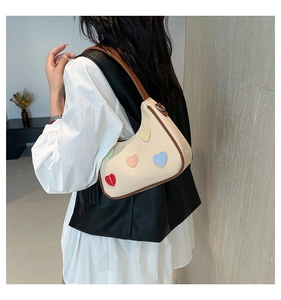 Detail of beige woven shoulder bag featuring colorful heart patches and brown leather trim