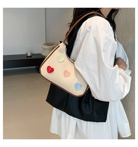 Close-up of beige woven underarm bag with four colorful heart patterns and brown leather strap