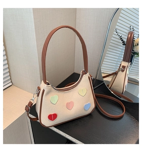 Detail of woven beige shoulder bag with colorful heart patches and brown leather trim