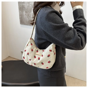 Detail of cream corduroy shoulder bag featuring red strawberry prints and metal plaque