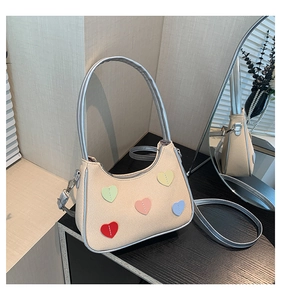 Detail of beige textured fabric shoulder bag with colorful heart patterns and silver strap
