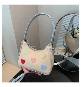 Detail of beige canvas underarm bag with colorful heart patches and silver strap