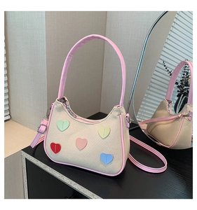 Detail of beige canvas shoulder bag with pink leather trim and colorful heart patches