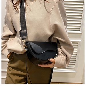 Detail of black saddle bag with wide fabric shoulder strap and gold-tone metal hardware