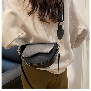 Detail of black saddle bag with matte PU finish, gold hardware, and wide woven strap