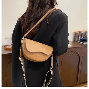 Brown leather saddle bag with wide shoulder strap shown on model in a cafe setting