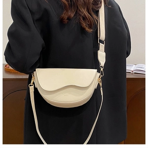 Detail of cream saddle bag with wave-curve flap and wide fabric shoulder strap worn by model