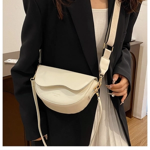 Detail of a beige saddle bag featuring a wavy flap and wide black-and-white strap
