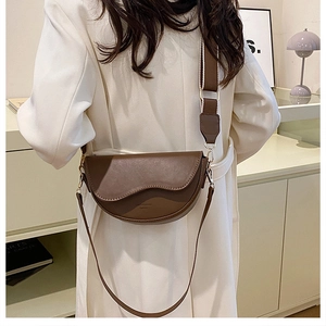 Detail of a dark brown saddle bag with wavy flap and wide fabric strap on a model