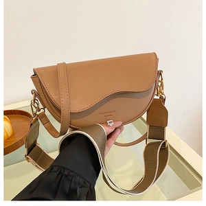 Detail of brown saddle bag with wide woven strap and adjustable faux leather shoulder strap
