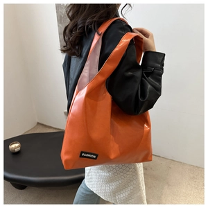 Detail of bright orange PU shoulder bag featuring a black fashion label and wide strap