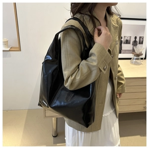 Close-up of black glossy PU leather tote bag with FASHION logo tag on beige suit outfit