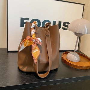 Brown litchi leather bucket bag with silk scarf and gold lettering on black surface