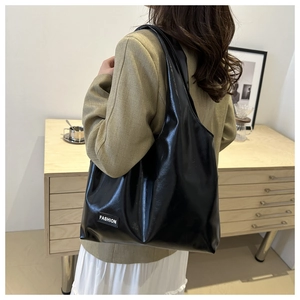 Detail of glossy black PU leather shoulder bag with FASHION label on model