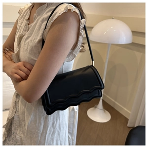 Detail of black underarm bag featuring scalloped edge design and gold hardware