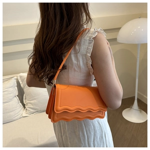 Detail einer hellorangen Schultertasche mit gewellter Klappe, getragen von einem Modell