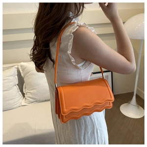 Close-up of bright orange crossbody bag featuring unique scalloped edges and silver hardware