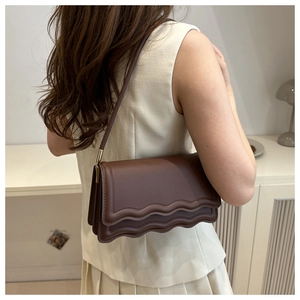 Detail view of a dark brown underarm bag featuring wave edge flap and matte leather texture