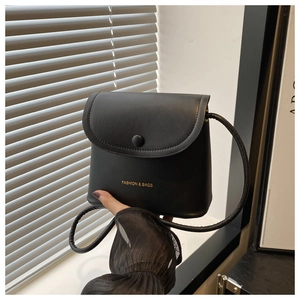 Detail of black mini crossbody bag featuring golden fashion text and magnetic flap closure