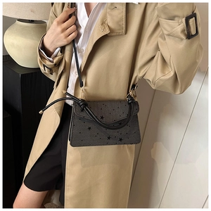 Detail of trendy crossbody bag featuring black star pattern and knotted top handle design
