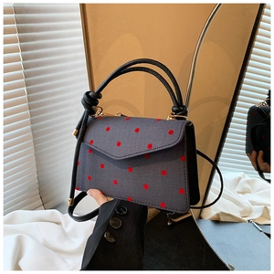Detail of grey polka dot handbag featuring a trapezoid shape and black round handle
