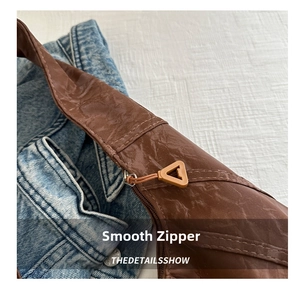 Detail shot of smooth zipper and textured pleated fabric on a brown shoulder bag