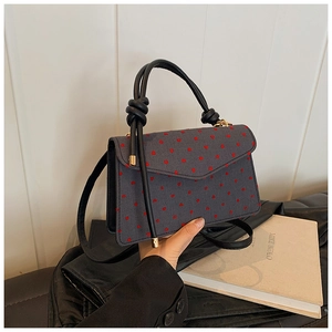 Detail of grey square crossbody bag with red heart pattern and black knotted handle