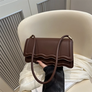 Brown leather crossbody bag with wavy edge detail and gold hardware held by hand