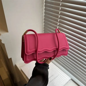 Magenta crossbody bag with wavy edge design and gold metal hardware held in hand