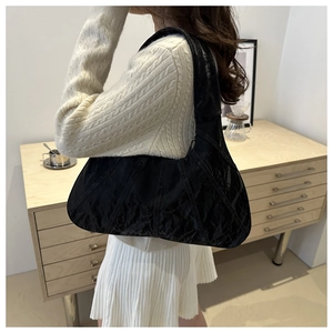 Detail of a black pleated leather shoulder bag with vertical stitching on a white sweater