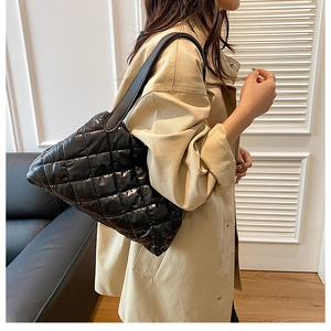 Close-up of black quilted puff tote bag with shiny finish and wide shoulder strap