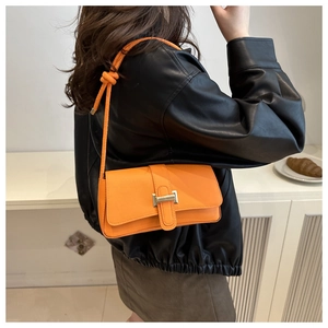 Detail of a bright orange crossbody bag with a silver buckle and knotted shoulder strap