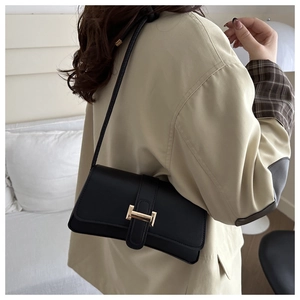 Detail shot of a black leather underarm bag with gold H-clasp on a beige coat outfit