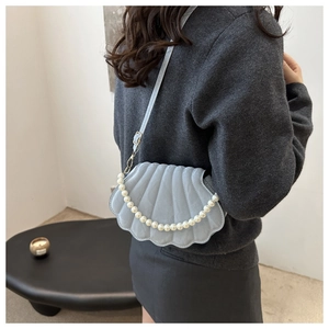 Detail of light blue shell-shaped crossbody bag with quilted texture and pearl chain
