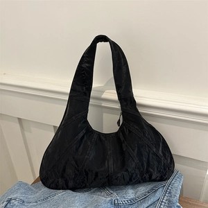 Minimalist black pleated tote bag with wide shoulder strap on denim surface
